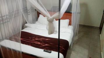 A bed with a canopy, a remote control on the bed, and a brown blanket.