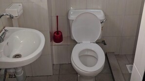 A small, clean bathroom with a white sink, toilet, and a red plunger. - Becca Hotel Meru (Meru)
