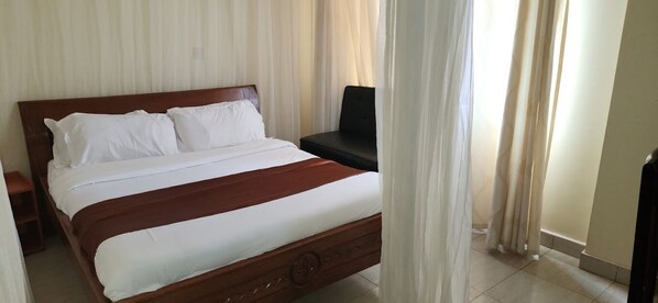 Un lit bien fait, avec du linge de lit blanc et une tête de lit marron, une table de chevet et une chaise noire.