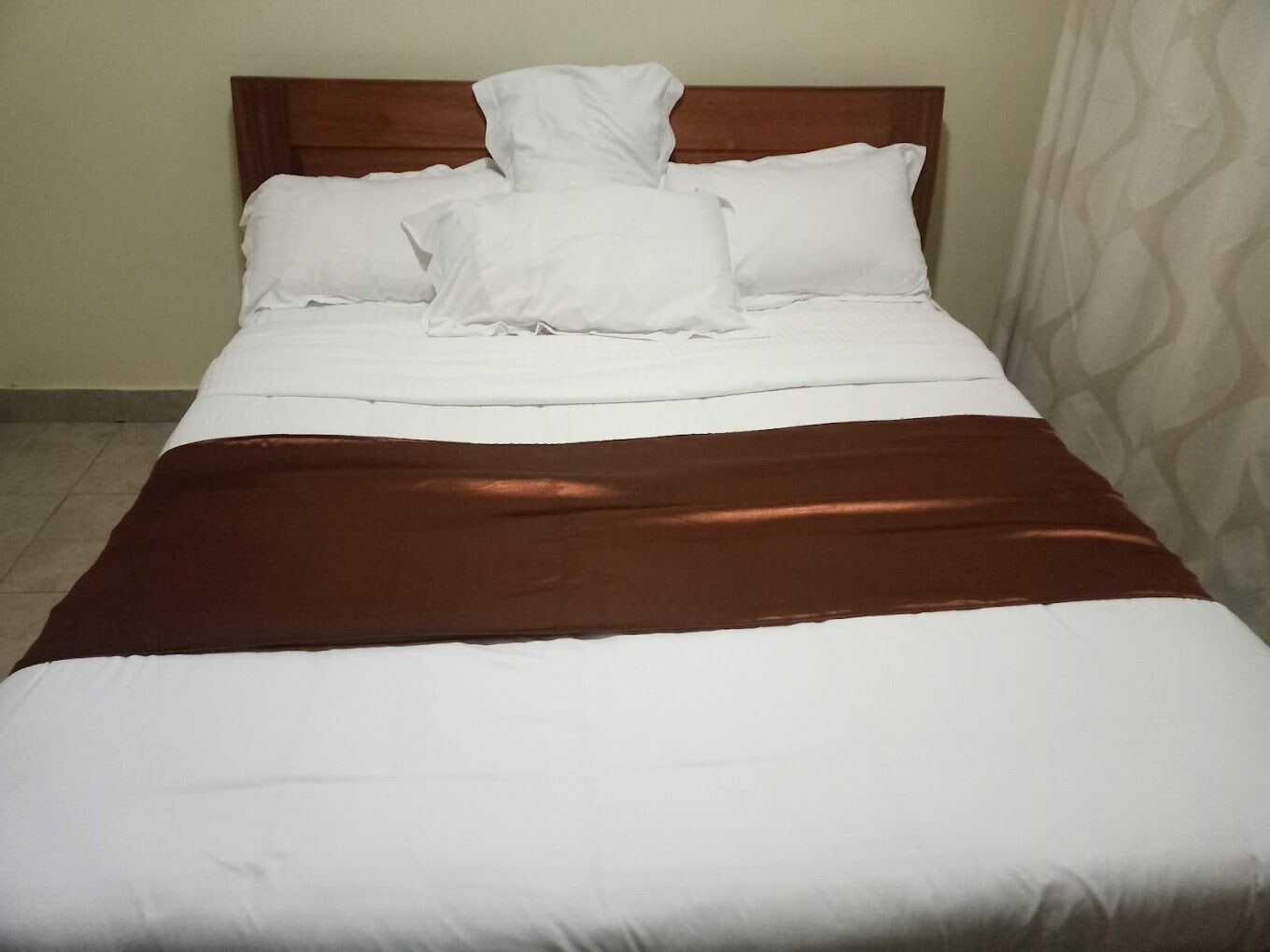 Una cama bien hecha con sábanas blancas y una manta marrón.