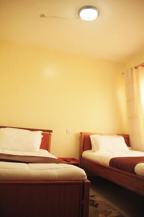Habitación de hotel con dos camas, cabeceros de madera y una lámpara en el techo.