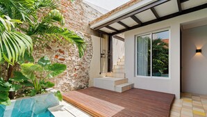 Uma área externa moderna com um deck de madeira, piscina e um muro de pedra.