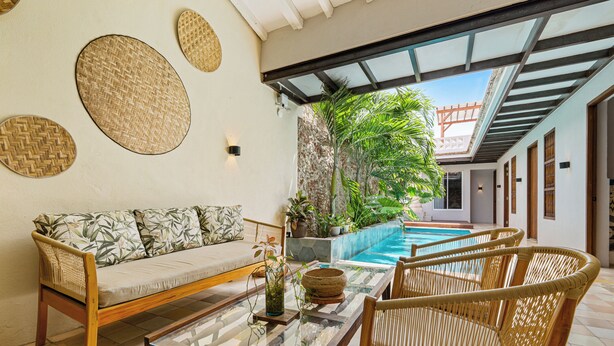 Uma área interna de piscina moderna com um sofá, cadeiras de vime e uma mesa de vidro.