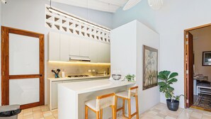Cozinha moderna com armários brancos, ilha central com banquetas, uma planta em vaso e uma obra de arte emoldurada na parede.