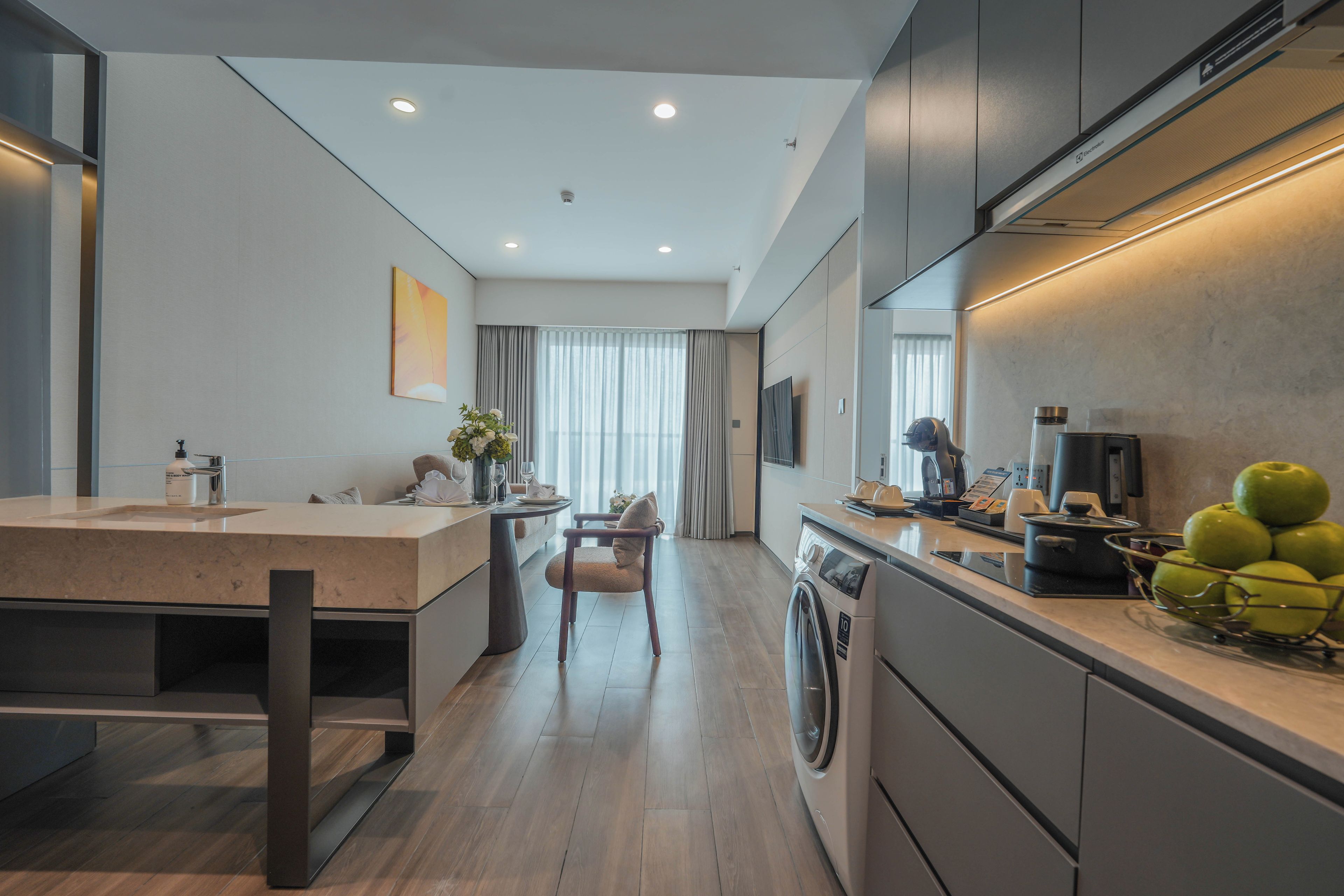 A modern kitchen with a built-in washing machine, a dining area with a table and chairs, and a large window with curtains.