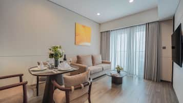 A modern hotel room with a dining area, a sofa, a TV, and a large window with curtains.