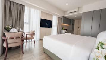 A hotel room with a bed, a desk with a chair, a television, and a kitchenette.
