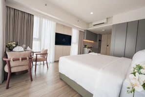A hotel room with a bed, a desk with a chair, a television, and a kitchenette.