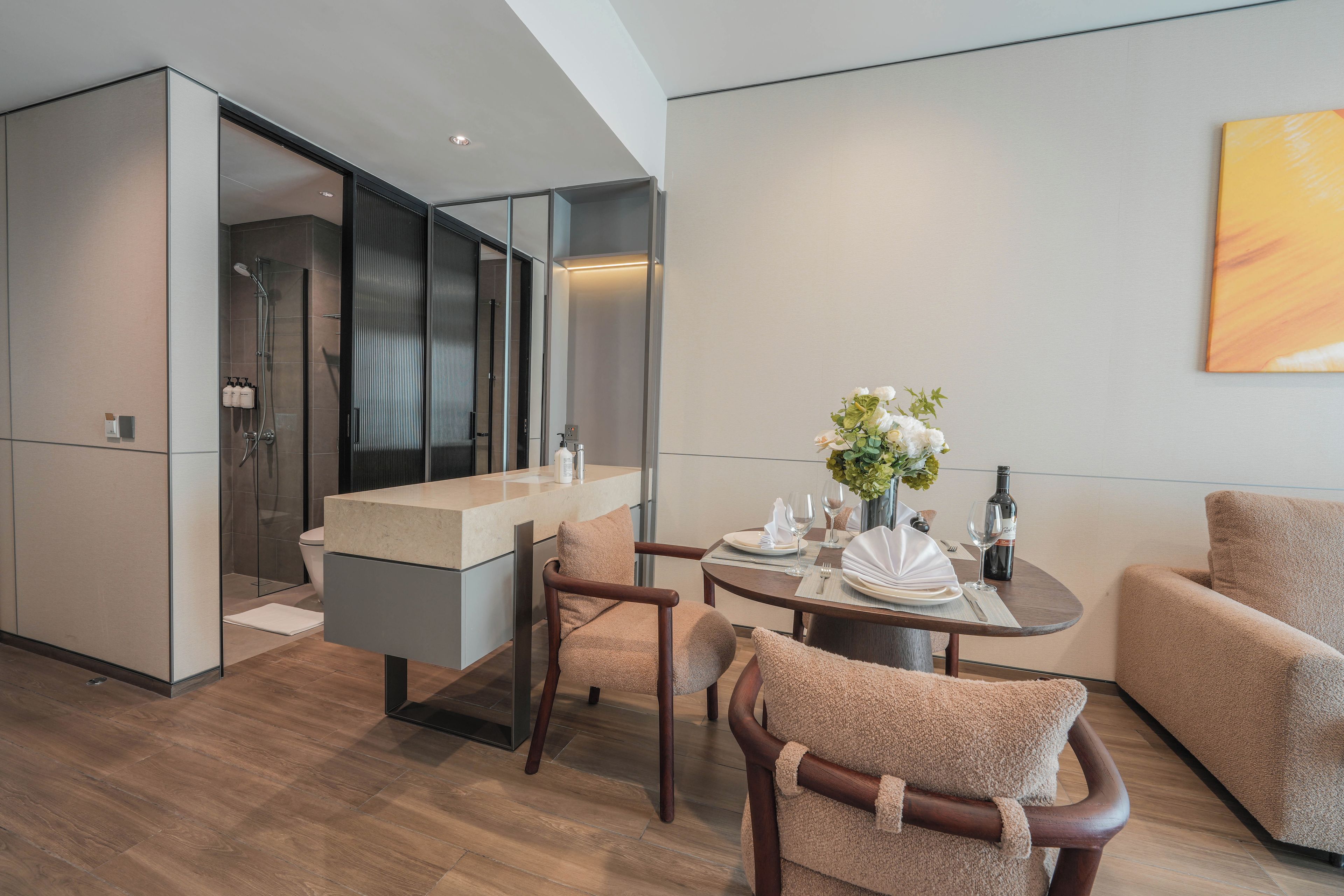 A modern hotel room with a dining area, a sofa, and a large window.