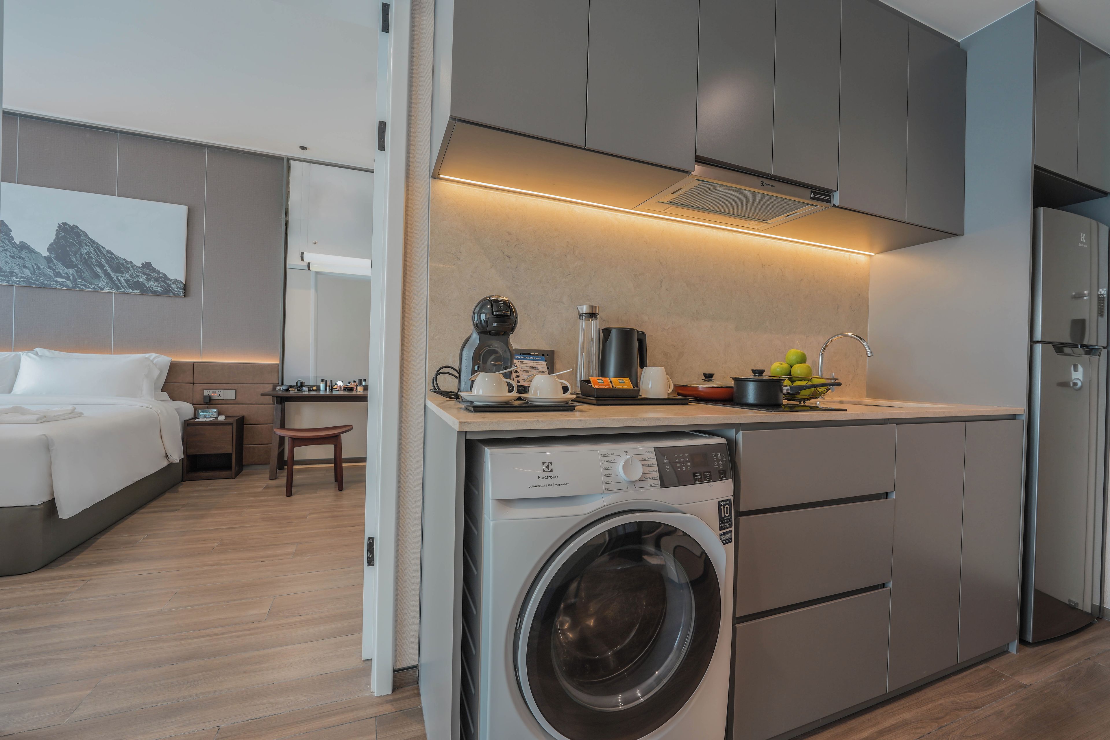 A compact hotel room with a kitchenette, a washing machine, and a bed.