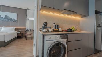 A compact hotel room with a kitchenette, a washing machine, and a bed.