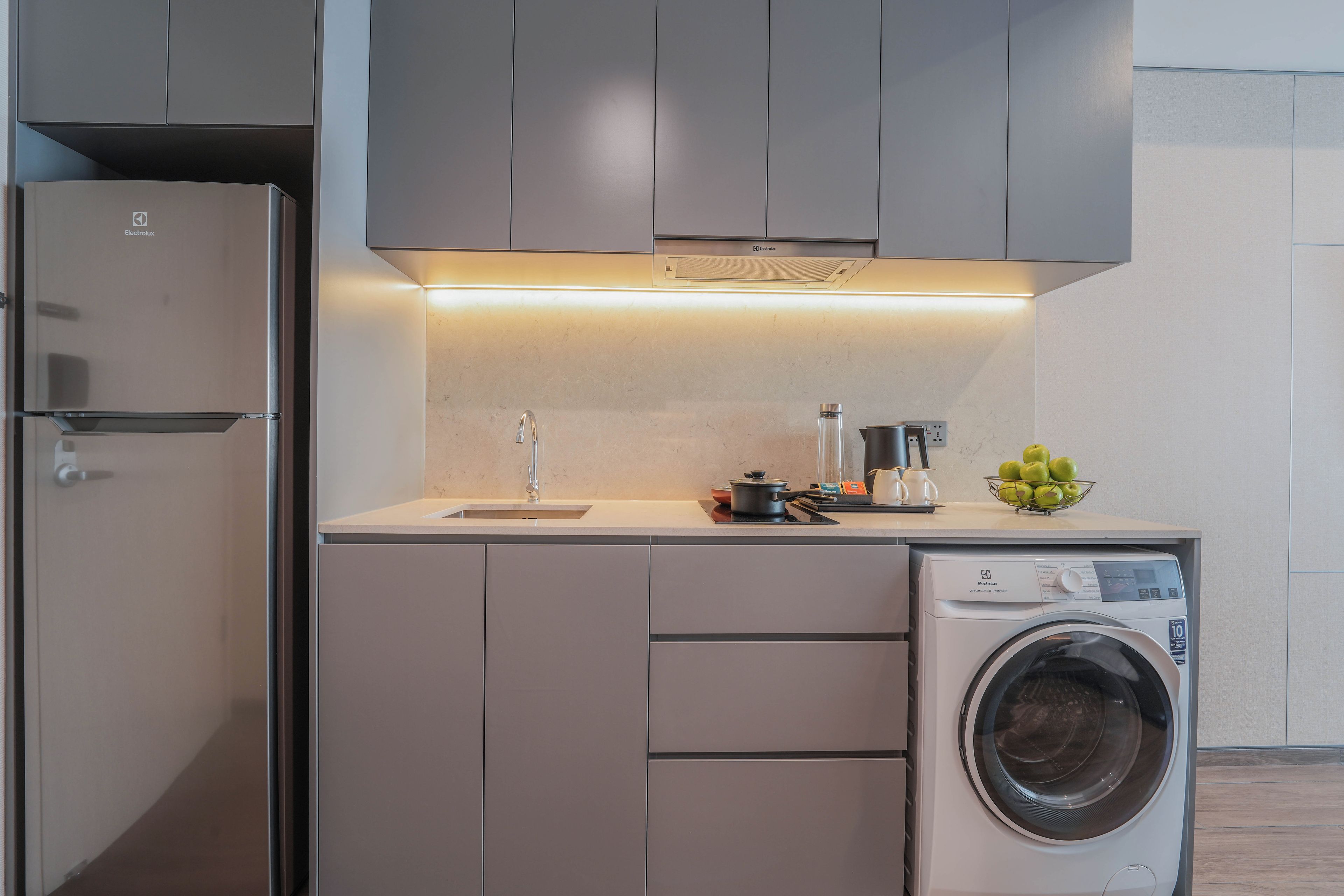 Cozinha compacta com máquina de lavar embutida, pia e bancada com uma tigela de maçãs.