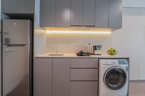A compact kitchen with a built-in washing machine, a sink, and a countertop with a bowl of apples.