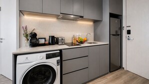 A compact kitchen with a built-in washing machine, a coffee maker, and a fruit bowl on the counter. - Residence on Opus Bay - Balmoral Tower Hotel (Batam)