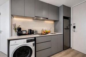 A compact kitchen with a built-in washing machine, a coffee maker, and a fruit bowl on the counter.
