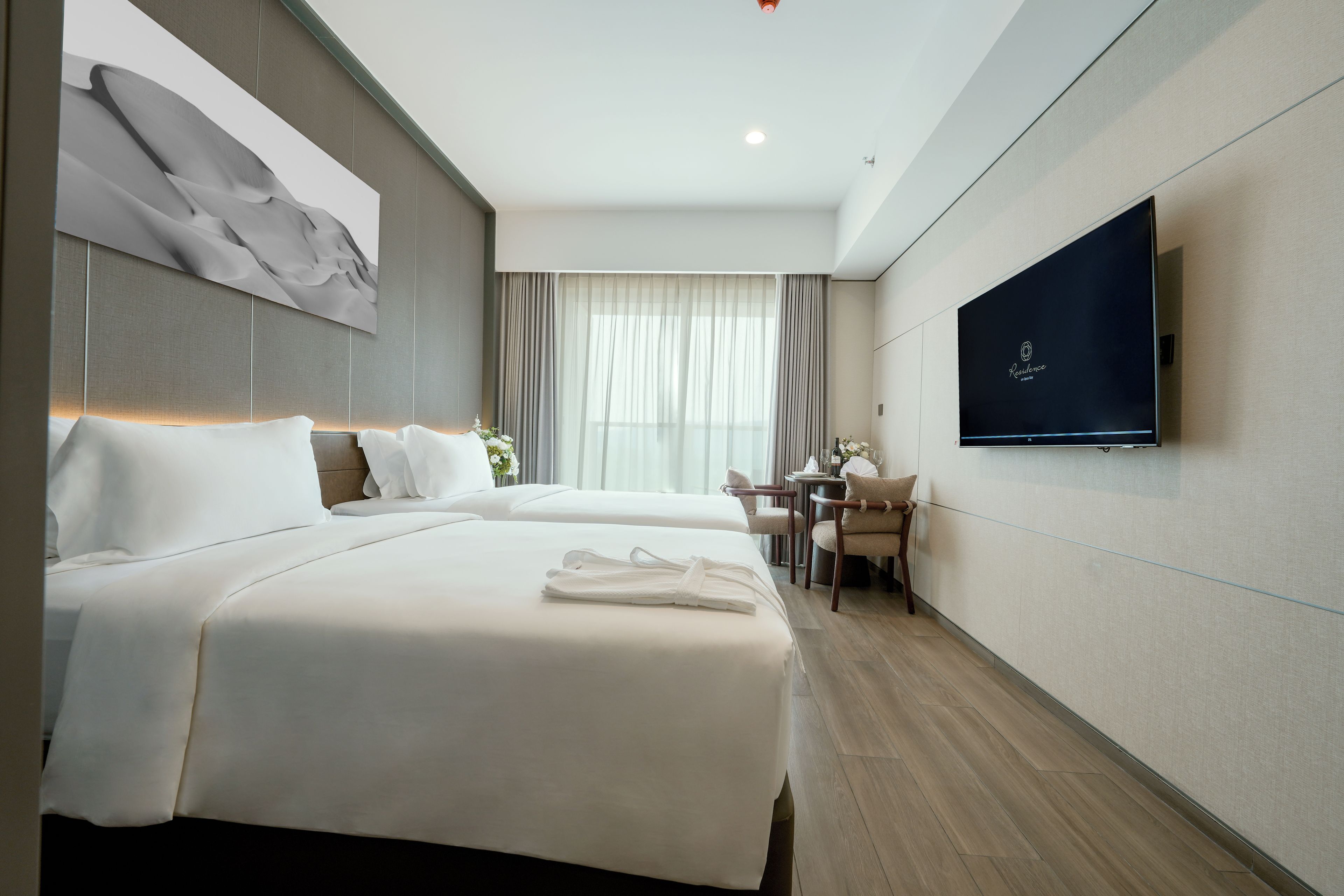 A hotel room with two beds, a TV on the wall, a desk with a chair, and a window with curtains.