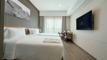 A hotel room with two beds, a TV on the wall, a desk with a chair, and a window with curtains.