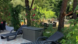 Een terras buiten met twee lounge stoelen en een kleine tafel, omringd door bomen en groen.