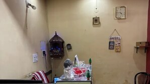 Une pièce avec un ventilateur de plafond, une horloge, une petite table ornée de quelques objets décoratifs et une chaise.
