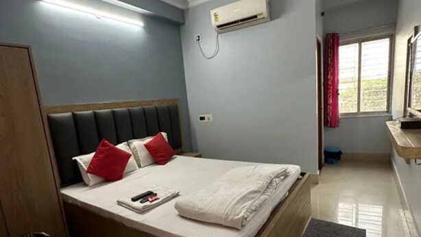 Une chambre à coucher comprenant un lit, une table de chevet, une armoire, un ventilateur de plafond, un appareil de climatisation et une fenêtre avec des rideaux.