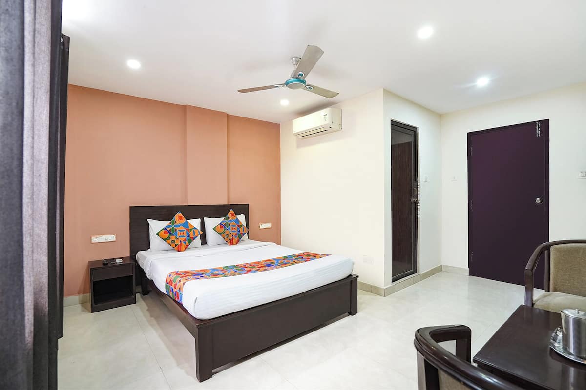 A modern hotel room with a bed, a desk, a chair, a ceiling fan, and a door.