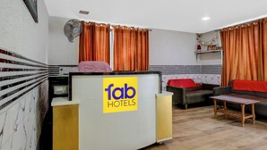 Ein Empfangsbereich mit einem ‚fab hotels‘ Schild, einer Couch, einem kleinen Tisch und orangenen Vorhängen.