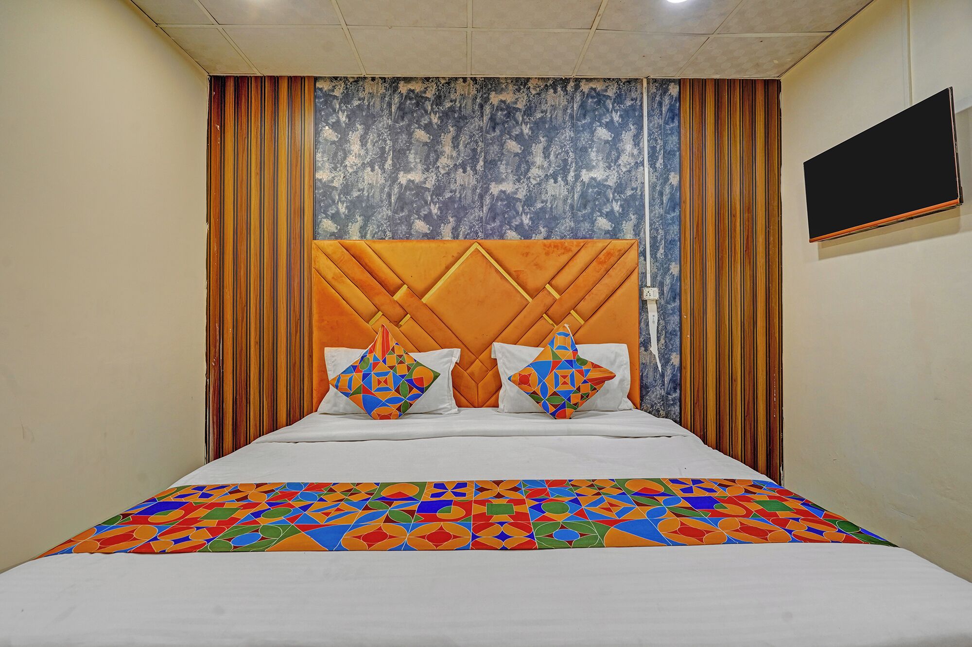 Una cama con colcha de estampado geométrico, cabecera capitonada y dos almohadas decorativas.