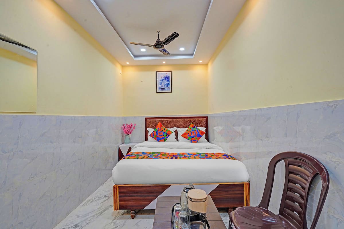 A bedroom with a bed, a chair, a ceiling fan, and a small table with a lamp.