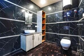 A modern bathroom with a white sink, wooden shelves, a marble backsplash, and a toilet. - Fabhotel Golden Mansion (New Delhi)