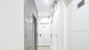A narrow hallway with white walls and a marble floor leading to a door marked with the number 404. - Via Lochav Residency (New Delhi)