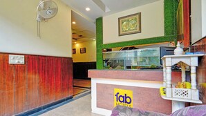A hotel reception area with a wooden reception desk, a glass display case, and a seating area with patterned cushions. - Fabhotel Smart Inn-1 (Gurugram)