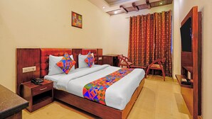 A hotel room with a wooden bed, a desk with a telephone, a chair, and a curtain. - Fabhotel Smart Inn-1 (Gurugram)