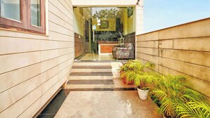 A modern building entrance with a glass door, a reception desk, and a patterned armchair. - Fabhotel Smart Inn-1 (Gurugram)
