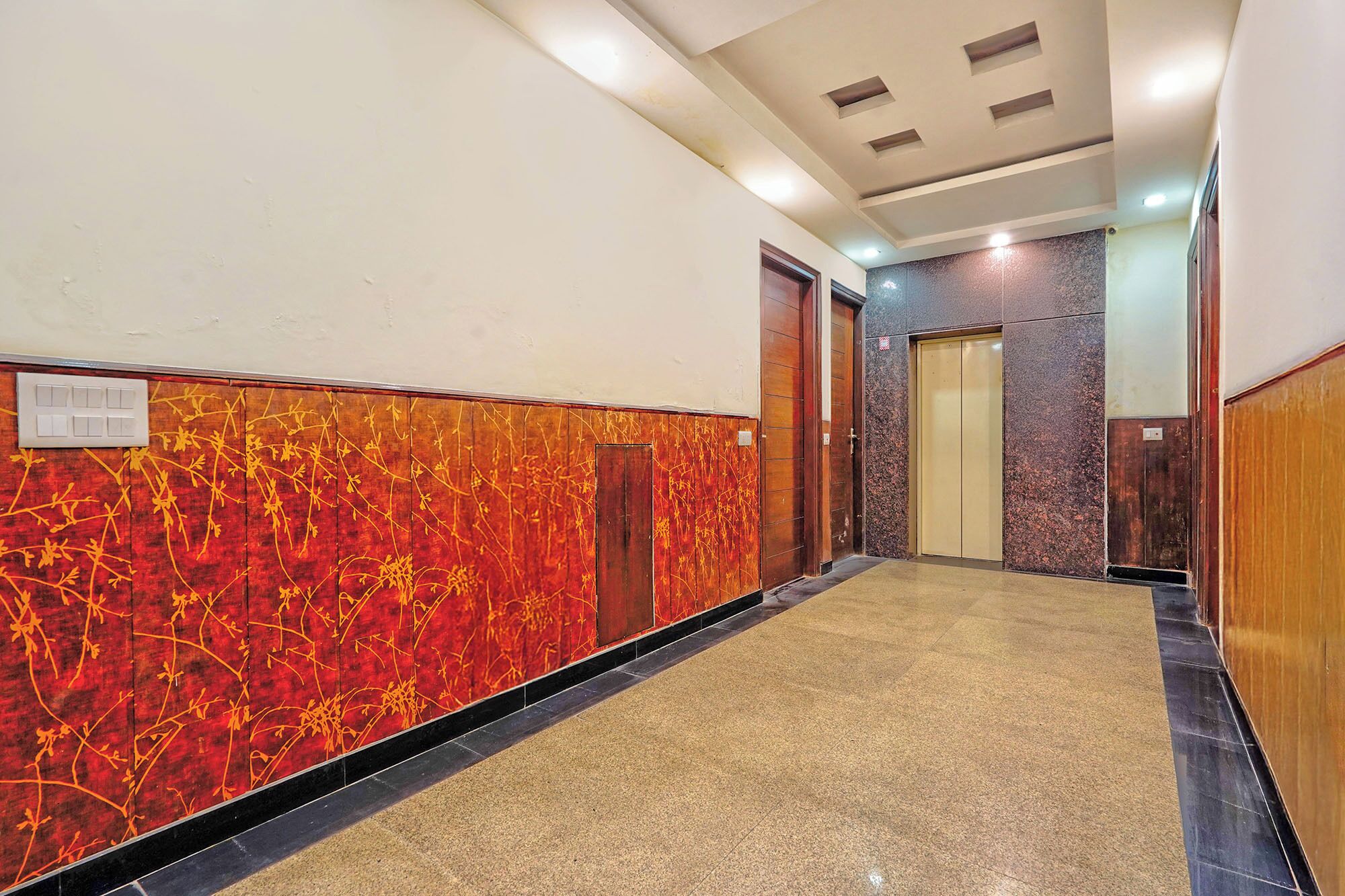 A hallway with a red and black patterned wall, a tiled floor, and a ceiling with recessed lighting.