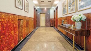 A hallway with a marble floor, wooden paneling, and a console table with a vase of flowers. - Fabhotel Smart Inn-1 (Gurugram)