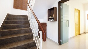 Eine Treppe mit hölzernem Geländer, ein an der Wand befestigtes Regal mit Dekoration und eine Tür zu einem weiteren Raum.