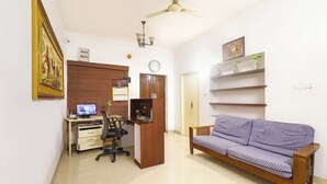 Ein Zimmer mit Schreibtisch, Stuhl, Sofa, Regalen und Deckenventilator.