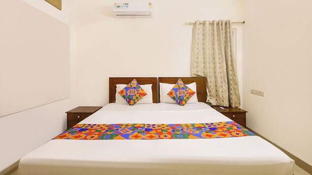 Une chambre d’hôtel comprenant un lit, deux oreillers, une table de chevet, un climatiseur fixé au mur et une fenêtre avec des rideaux.