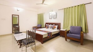 Ein Hotelzimmer mit Bett, Schreibtisch, Stuhl, Nachttisch und Deckenventilator.