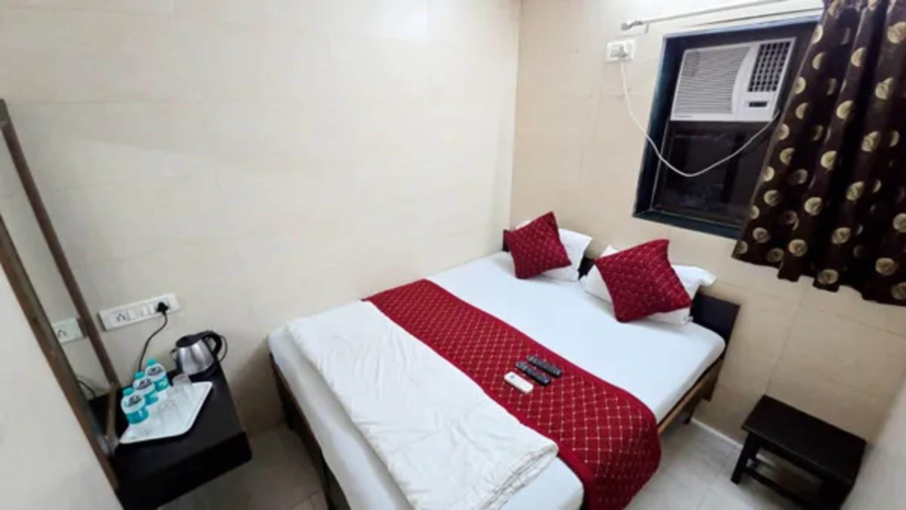 A small, clean room with a bed, a nightstand, a window with curtains, and a wall-mounted air conditioner.