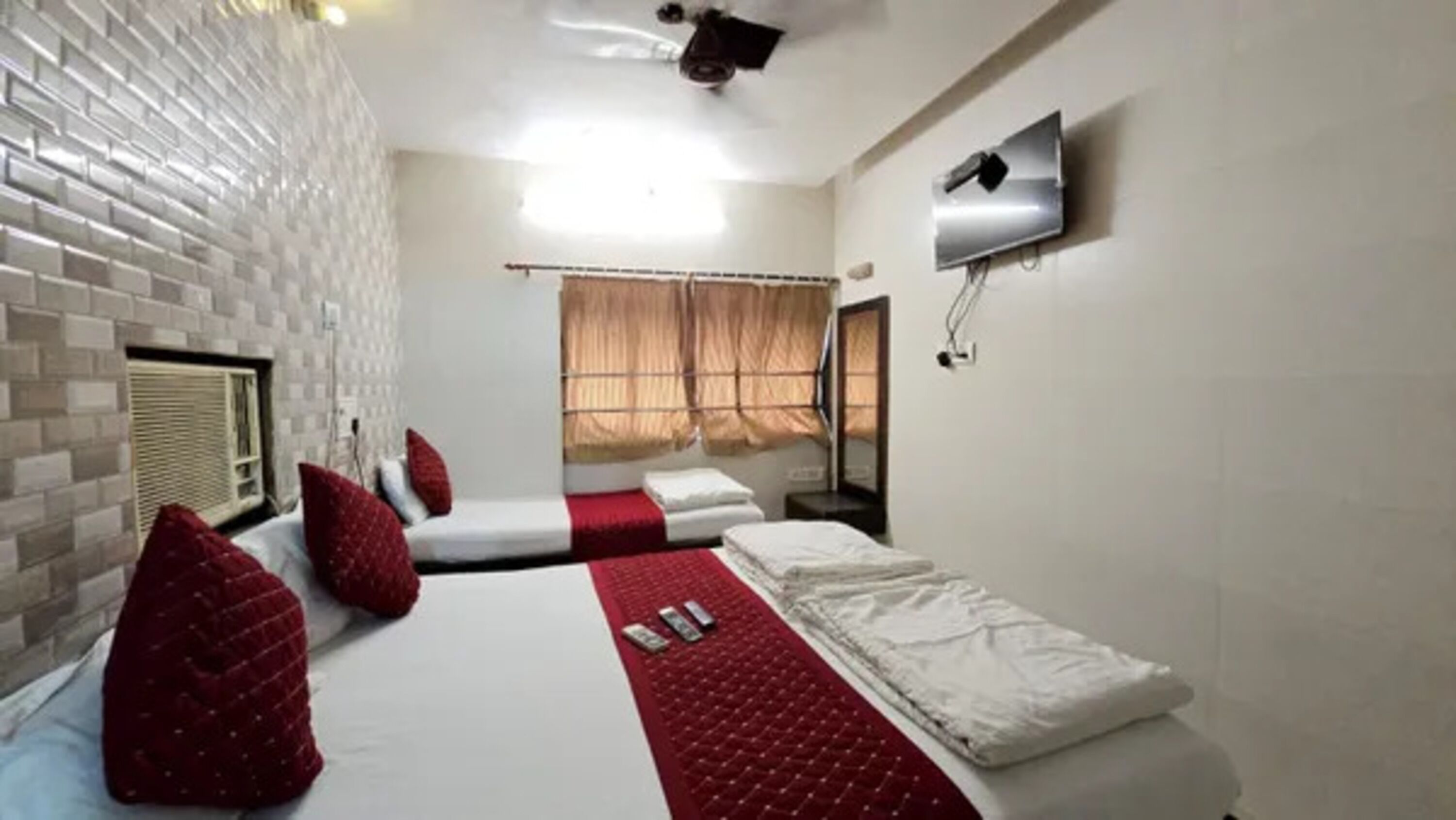 A hotel room with two beds, a TV mounted on the wall, and a window with curtains.