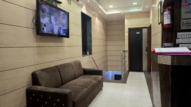A lobby with a brown sofa, a television mounted on the wall, a reception desk, and a fire extinguisher. - Fabhotel Kamal (Mumbai)