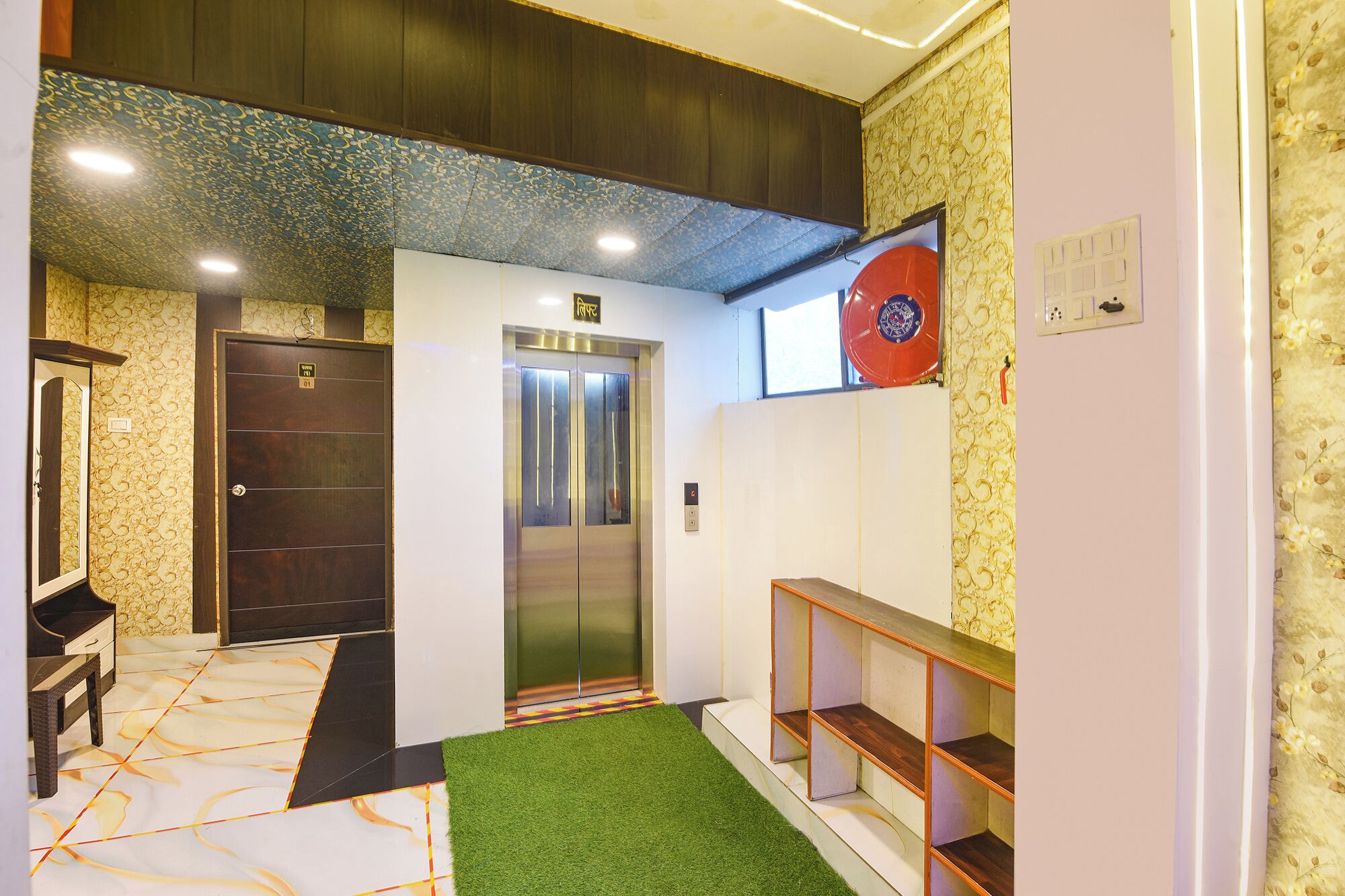 A hotel lobby with an elevator, a reception desk, and a green artificial turf area.