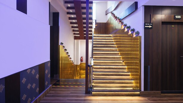 Un hall d’hôtel moderne avec un escalier, un comptoir d’accueil et un panneau indiquant les numéros de chambre 105 et 107.