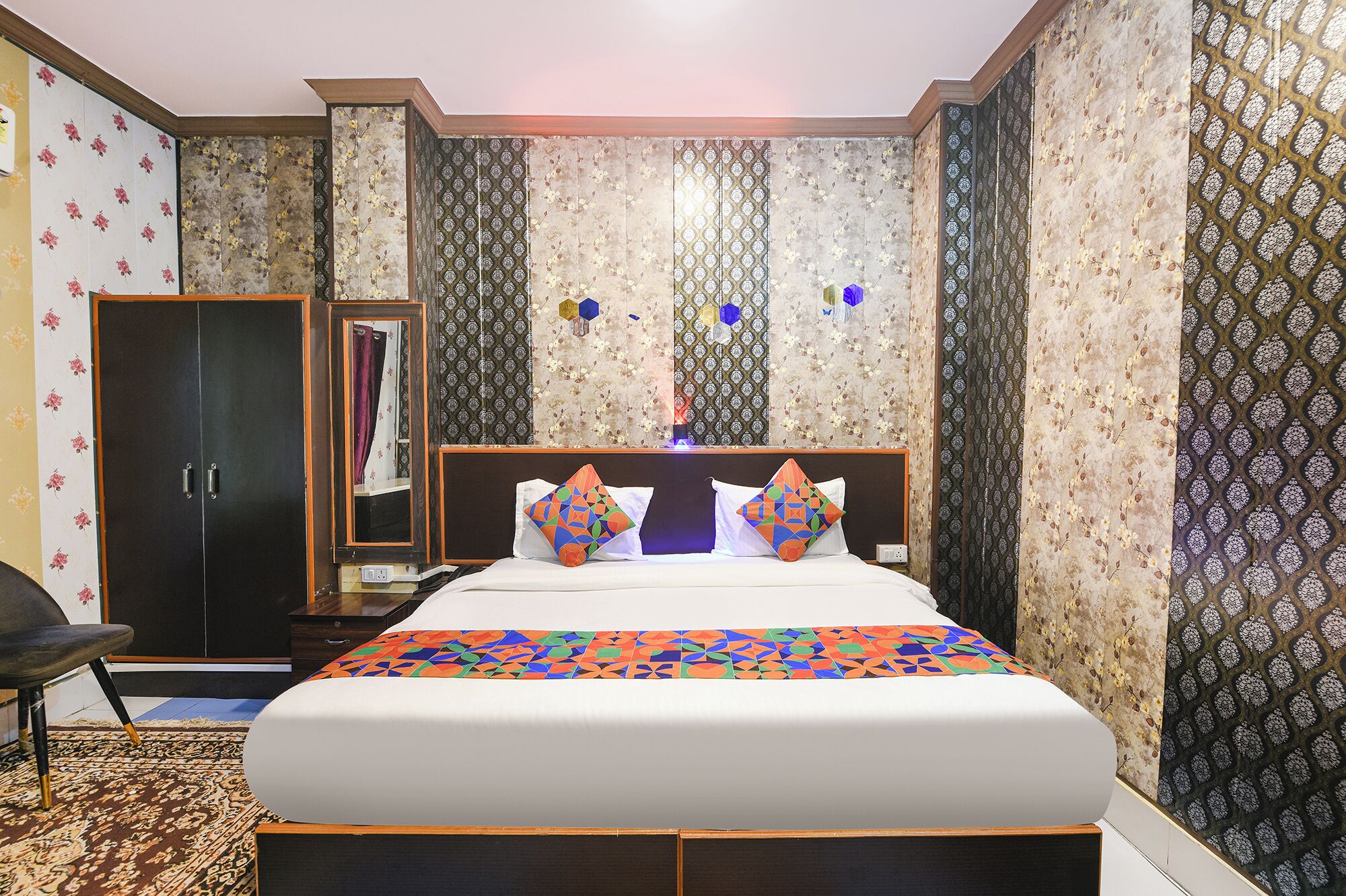 Una habitación de hotel con una cama grande, un armario, un espejo y papel tapiz estampado.