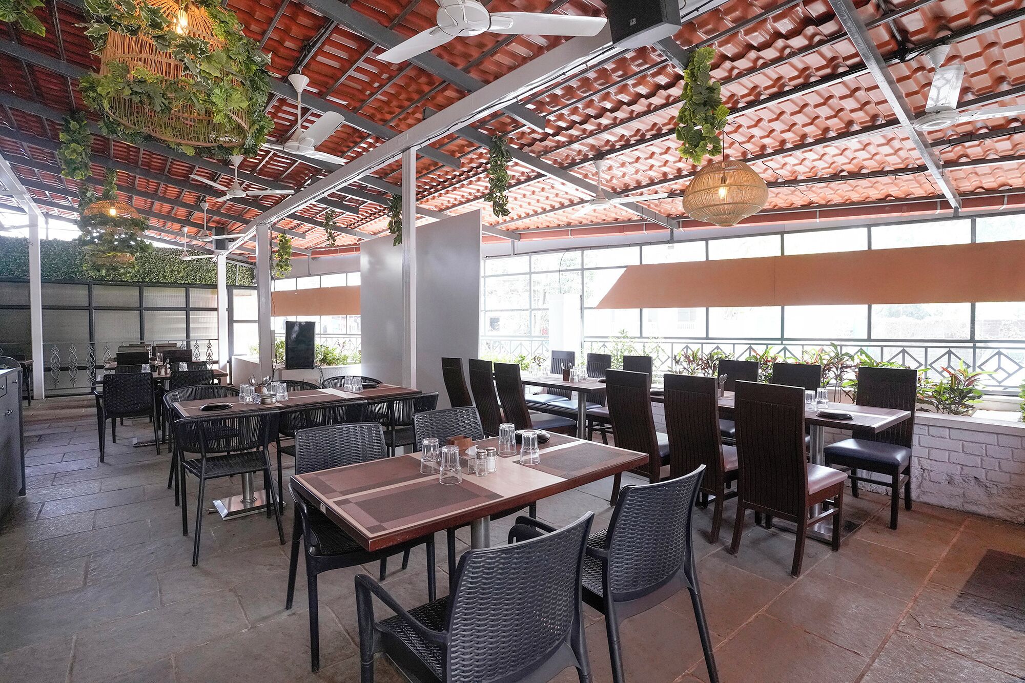 An indoor dining area with tables and chairs, a high ceiling with a red-tiled roof, and large windows allowing natural light.
