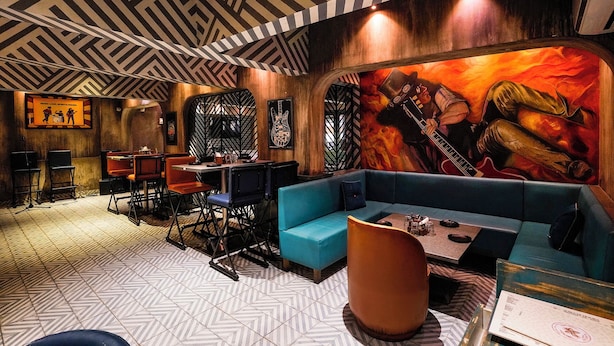 Un ristorante con un soffitto a motivi geometrici, un murale raffigurante un chitarrista e un assortimento di posti a sedere, tra cui un divano blu e sedie.