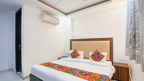 Habitació d'hotel amb llit, ventilador de sostre, aparell d'aire condicionat, tauleta de nit i finestra amb cortines.