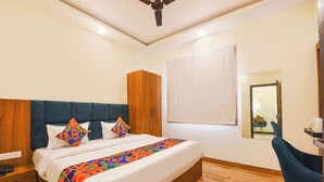 A hotel room with a large bed, a wooden headboard, a desk with a chair, and a mirror. - Fabhotel Haritaj (Varanasi)