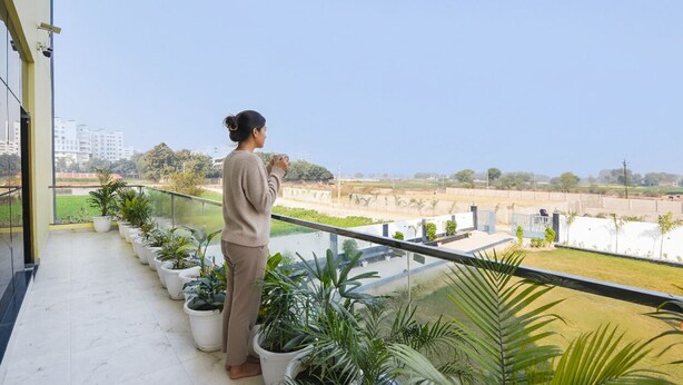 A balcony with potted plants, a clear view of the surrounding area, and a person standing on the balcony. - Fabhotel Haritaj (Varanasi)